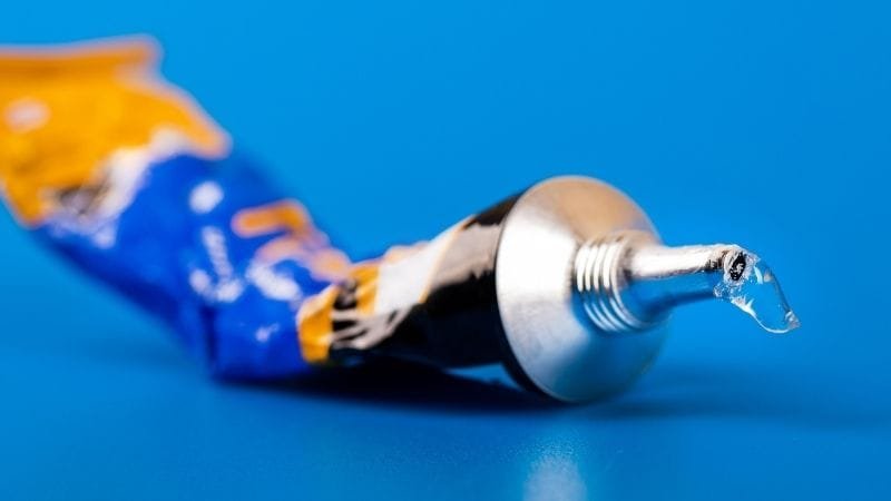 Tubo de pegamento y adhesivo epóxico industrial sobre superficie neutra.